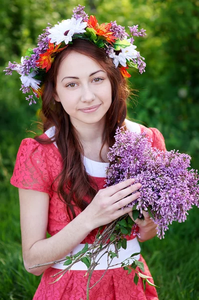 Beautiful woman with a bouquet of lilac in a wreath — Stock Photo, Image