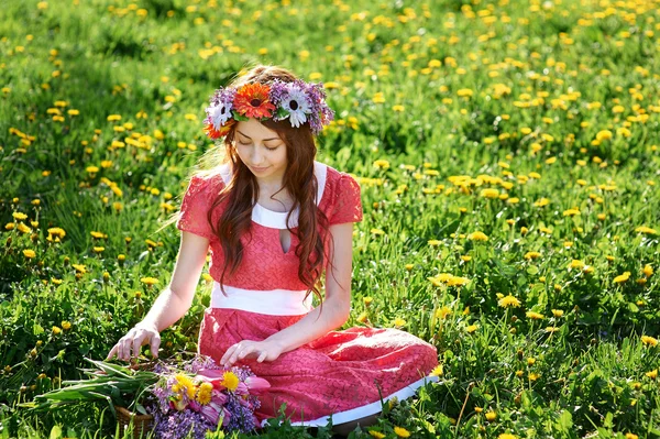 牧草地の草の上に座って花輪を持つ美しい女性 — ストック写真