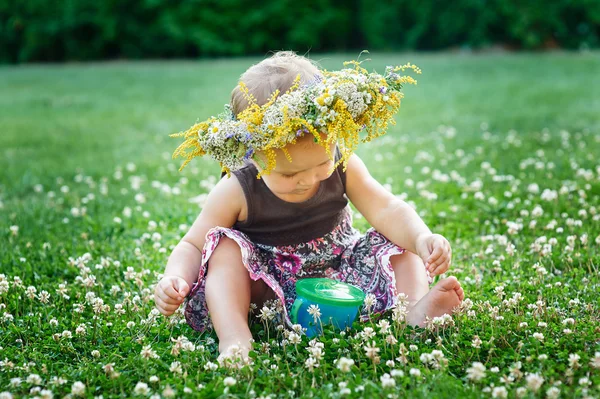 Vacker glad liten baby flicka i en krans på en äng på natur — Stockfoto