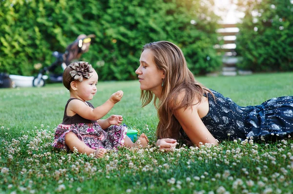 Junge Mutter und ihre kleine Tochter spielen auf Gras — Stockfoto