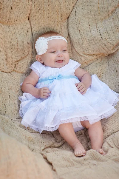 小さな女の赤ちゃんは、白い椅子をポーズします。彼女は幸せそうに笑っています。 — ストック写真