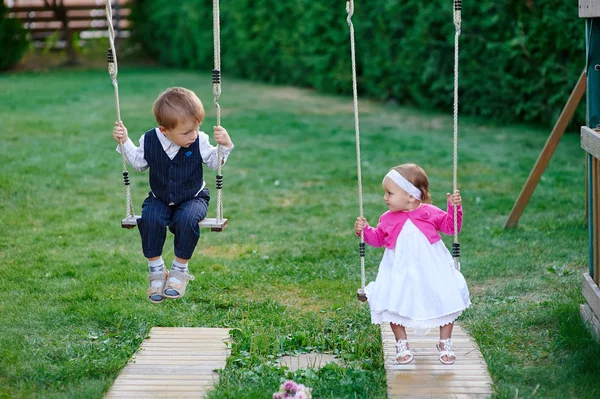 Маленький хлопчик і дівчинка катаються на гойдалці на дитячому майданчику в парку — стокове фото