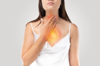 A woman suffering from acid reflux or Heartburn on gray Background clipart