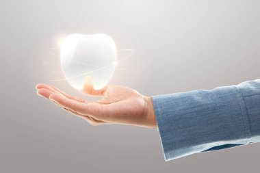 Dişçi elleri açık gri arka planda beyaz dişler gösteriyor. Diş bakımı ve koruma kavramı