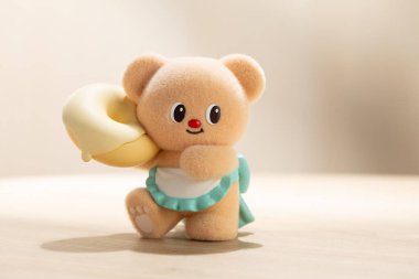 Masaya yerleştirilmiş büyük bir donut tutan sevimli bir ButterBear oyuncağının arka plan fotoğrafı. Ilık ışık, neşeli ve büyüleyici kavramlar için uygun yumuşak, rahat bir ortam yaratır..