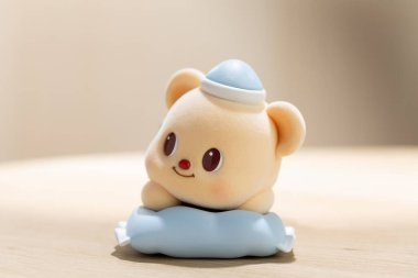 ButterBear sanat oyuncağı yumuşak mavi bir yastığın üzerinde rahatlatıcı gösterilir, sevimli karakter tasarımı, sakin ruh hali ve modern yaşam tarzı görselleri için kolektif cazibe vurgulanır.