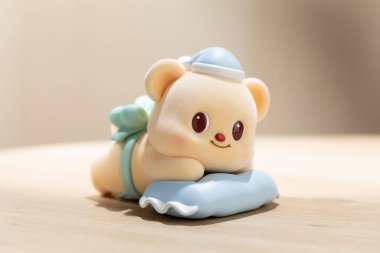 ButterBear sanat oyuncağı yumuşak mavi bir yastığın üzerinde rahatlatıcı gösterilir, sevimli karakter tasarımı, sakin ruh hali ve modern yaşam tarzı görselleri için kolektif cazibe vurgulanır.