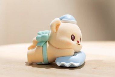 ButterBear sanat oyuncağı yumuşak mavi bir yastığın üzerinde rahatlatıcı gösterilir, sevimli karakter tasarımı, sakin ruh hali ve modern yaşam tarzı görselleri için kolektif cazibe vurgulanır.