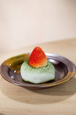 Yumuşak ve çiğnenmiş kiraz mochi üzerine taze çilek konmuş, kırsal seramik tabakta servis ediliyor. Doğal renkleri ve hassas dokuyu vurgulayan en az Japon tatlısı..