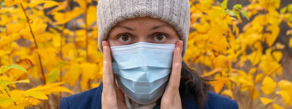 A girl adjusts a medical mask in an autumn Park. Coronavirus in the fall