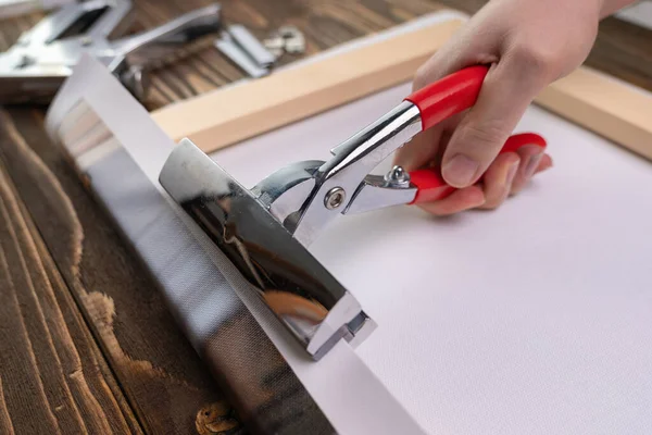 Hand with a tool for stretching the canvas. The business of producing paintings on canvas from photographs