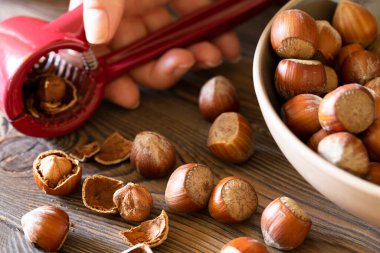 Hazelnuts with a red nutcracker in a bowl on a wooden board, nutshell, dark photo.