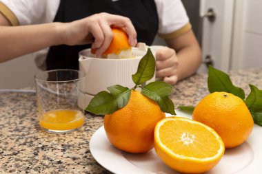 Mutfakta elinde portakal suyu ve taze narenciye ile meyve sıkacağı tutan bir kız.