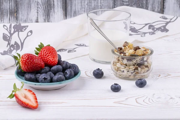 Gesundes Frühstück mit Müsli und frischen Erdbeeren und Blaubeeren, Milch auf weißem Holztisch im rustikalen Stil, Nahaufnahme, waagerecht — Stockfoto