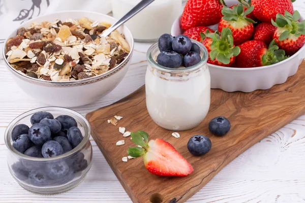 Здоровый завтрак с домашним йогуртом и свежей клубникой и черникой, мюсли на белом деревянном столе в деревенском стиле, близко, горизонтально — стоковое фото