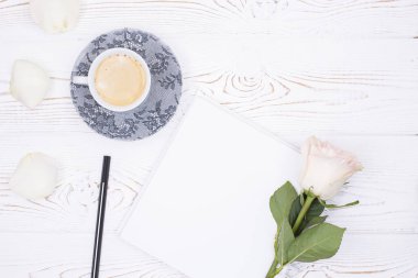 Kahve fincanının üst görüntüsü, boş defter, kalem, kırsal tarzda beyaz bir masada beyaz bir gül çiçeği. Düz yat, boşluğu kopyala