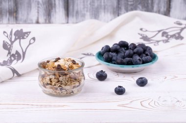 Müsli ve taze yaban mersinli sağlıklı kahvaltı beyaz ahşap bir masa üzerinde, kırsal tarzda, yakın plan, yatay.