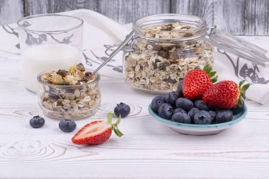 Tahıl gevreği ve sütle sağlıklı kahvaltı, beyaz ahşap bir masada yaban mersini ve taze çilek, kırsal tarzda, yakın çekim, yatay