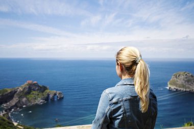 Kot ceketli yalnız bir sarışın İspanya 'nın Biscay Körfezi' nde denize ve kayalara bakıyor. Seçici odaklanma. Boşluğu kopyala