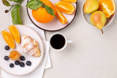Bir fincan kahveyle kahvaltı, taze kruvasan, reçel ve olgun yaban mersini ve sulu portakallar, beyaz armutlar, düz bir zemin, kopyalama alanı.