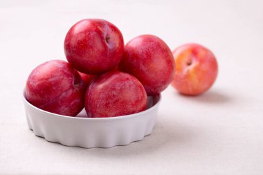 Masanın üzerinde beyaz bir seramik kasede açık keten masa örtüsü olan kırmızı erik. Sağlıklı organik hasat