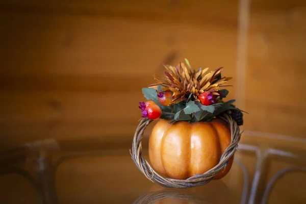 Decorative pumpkin decorated with leaves and berries on a glass table on a wooden background. Copy space — Stock Photo, Image