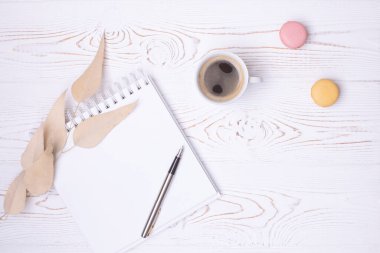 Yaylı boş bir günlükten, bir fincan kahveden, badem kurabiyesinden ve bej rengi kuru yapraklardan oluşan beyaz, köhne bir ahşap masa. Konforlu düz yerleşim