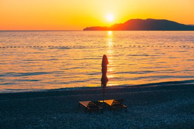 Alacakaranlıkta plajda dinlenme odası ve şemsiye. Denizin üstünde muhteşem bir gün batımı. Alacakaranlıktaki ada  