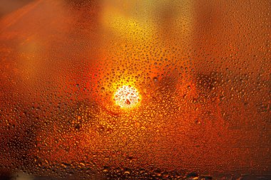 Arka planda parlayan günbatımına sahip bardağa damlalar