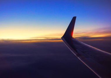 Kara bulutların üzerinde bir uçak kanadı. Alacakaranlıkta uçan uçak. Uçak penceresinde müthiş bir manzara