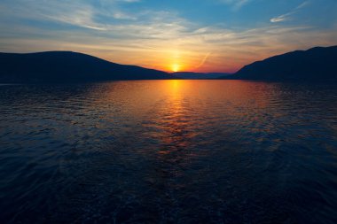 Deniz ve dağların üzerinde genel gün batımı. Deniz suyunda gün batımı yansıması