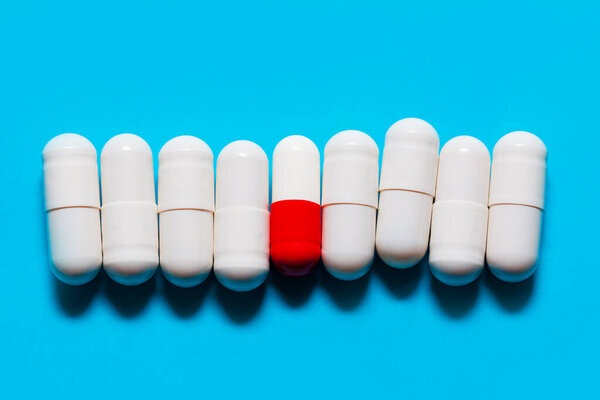 White Probiotic Capsules . One Red and White Capsule between White Capsules . Drugs at blue background . Pills in a row