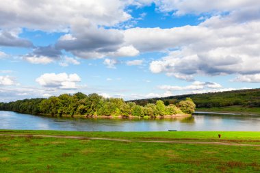 Kırsal nehir manzarası. Yeşil adanın üzerinde alçak bulutlar. Yeşil sahilde otlak 