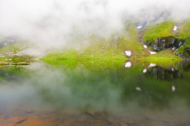Dağlarla birlikte gölün üzerinde sis var. Transfagarasan Romanya 'daki Balea Gölü