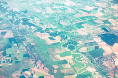 Dolambaçlı bir nehrin havadan görünüşü tarımsal tarlaların arasında dönüyor. Yüksek açılı su baskını perspektifi dikdörtgen çiftlik planlarıyla karakterize edilir.