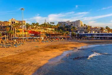  Playa de la Pinta Costa Adeje, Tenerife 'de, Kanarya Adaları' nda altın kum ve sakin bir deniz. Palmiye ağaçları, otellerin ve diğer binaların önündeki kumsalda kuyruk oluşturur.