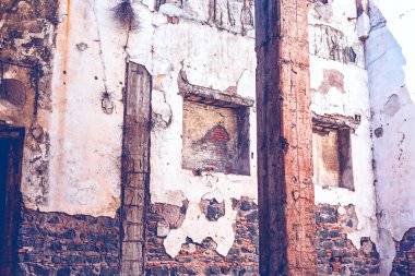 Yıpranmış alçı cephesi, gölgeli oyukta kırsal tuğlaları ve sağlam ahşap kirişleri ortaya çıkarıyor. Soluk oyuklar ve karanlık bir kapı aralığı terk edilme ve erozyonla ilgili hikayeler fısıldıyor. Yıpranmış dış görünüş 