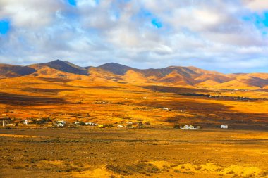 İspanya, Fuerteventura 'daki Valle de Santa Ines' in çorak çöl manzarası. Manzara kuru dağlar, küçük beyaz binalar ve bulutlu bir gökyüzü içerir.