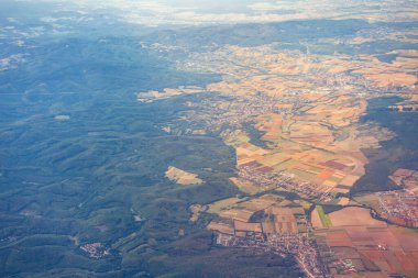 Orman tepeleri ekilmiş tarlalara ve uzak kentsel yayılıma, katmanlı doğa ve gelişim manzarasına karışıyor. Virajlı yollar ve kırsal kümeler vahşi doğadan yapısal yapıya geçiş izleri taşıyor.