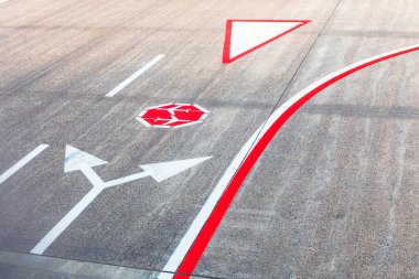 Havaalanının asfalt yüzeyine kılavuz işaretleri çizmiş. Araçlar için yön okları, zorunlu dur işareti, ve uçak kuyrukları.