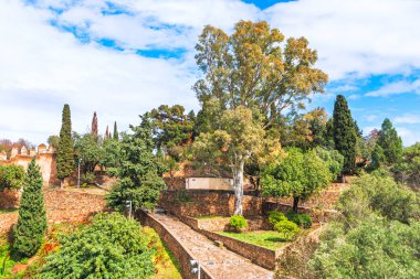 İspanya, Malaga 'da Castillo de Gibralfaro, gökyüzünün altında taş duvarlar ve yemyeşil bahçeler sergiliyor. Şehre tepeden bakan tarihi tahkimatlar ve bol miktarda Akdeniz bitkisi