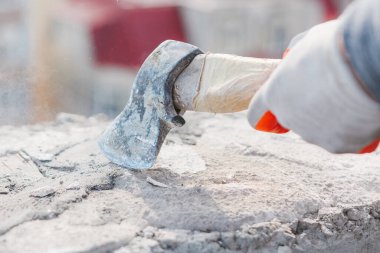 İş eldiveni giyen kişi beton enkaz yığınını parçalamak için balta kullanır. Darbe aracın vuruş noktası etrafında toz ve ince gri toz tekmeler