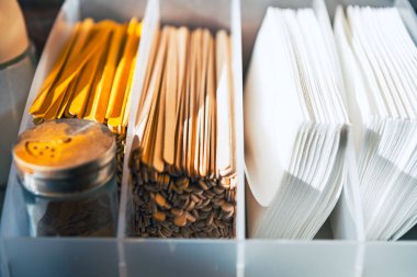 Ahşap karıştırıcıları, altın kaşıkları, beyaz plastik çatalları ve kompartımanlarında baharat karıştırıcısı olan organize restoran çeşni istasyonu, temiz modern kafe veya paket servis konsepti