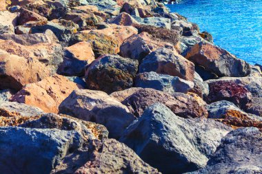 Yıpranmış kayalar kıyı şeridini okyanus dalgalarına karşı koruyan engebeli bir kıyı bariyeri oluşturur. Denize bitişik düzensiz kayaları gösteren taş yapı.