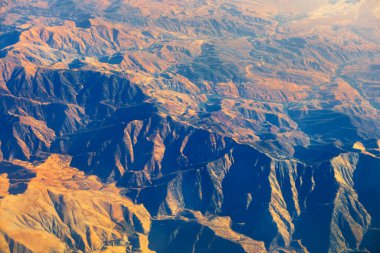Yukarıdan And Dağları 'nın manzarası. Uçsuz bucaksız bir manzara, derin mavi gölgeleri gösteren bir uçak penceresinden görülüyor.