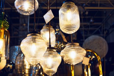 Kaburgalı cam kolye ışıkları showroom 'da sıcak bir şekilde parlar, her armatür şekil ve boyutta ince farklar gösterir. Çeşitli etiketler sallanıyor, satılık olup olmadıklarına dair ipuçları