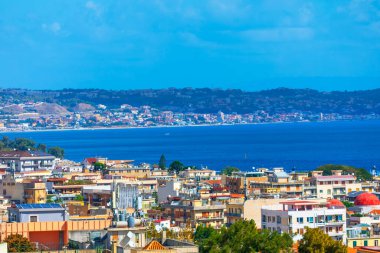 Messina Boğazı 'nın mavi sularına bakan Sicilya, Messina şehrinin panoramik manzarası. Canlı şehir binaları ve renkli çatılar denize açılıyor ve Calabria uzaktan görülebiliyor.