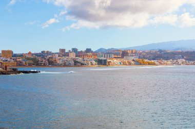 Las Palmas de Gran Canaria, İspanya 'daki geniş Las Canteras Sahili, su kenarında şehrin ufuk çizgisini gösteriyor. Sakin Atlantik Okyanusu uzun bir kıyı şeridine ve uzak dağlara çıkıyor.