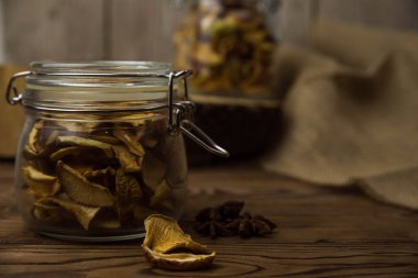 Ev yapımı kavrulmuş, kurutulmuş organik elma dilimleri. Kahverengi ahşap zemin üzerinde cam kavanozda baharat bulunan elma cipslerini metin için kopyalama alanı ile kapat