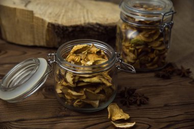 Ev yapımı kavrulmuş, kurutulmuş organik elma dilimleri. Kahverengi ahşap zemin üzerinde cam kavanozda baharat bulunan elma cipslerini metin için kopyalama alanı ile kapat